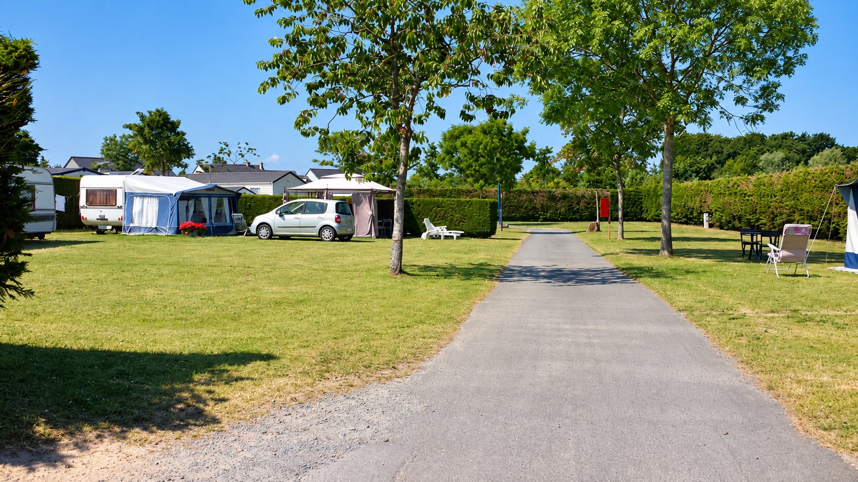 Allée du camping La Ville Es Poulains entre pelouses, arbres et emplacements de caravanes.