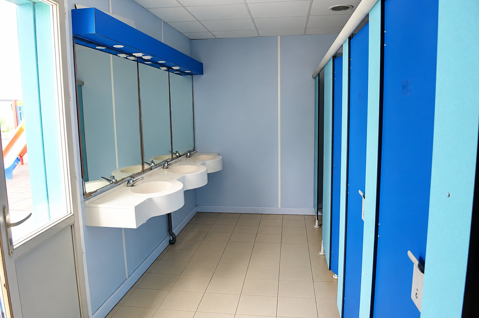 Bloc sanitaire modulaire avec lavabos blancs et cabines bleues.