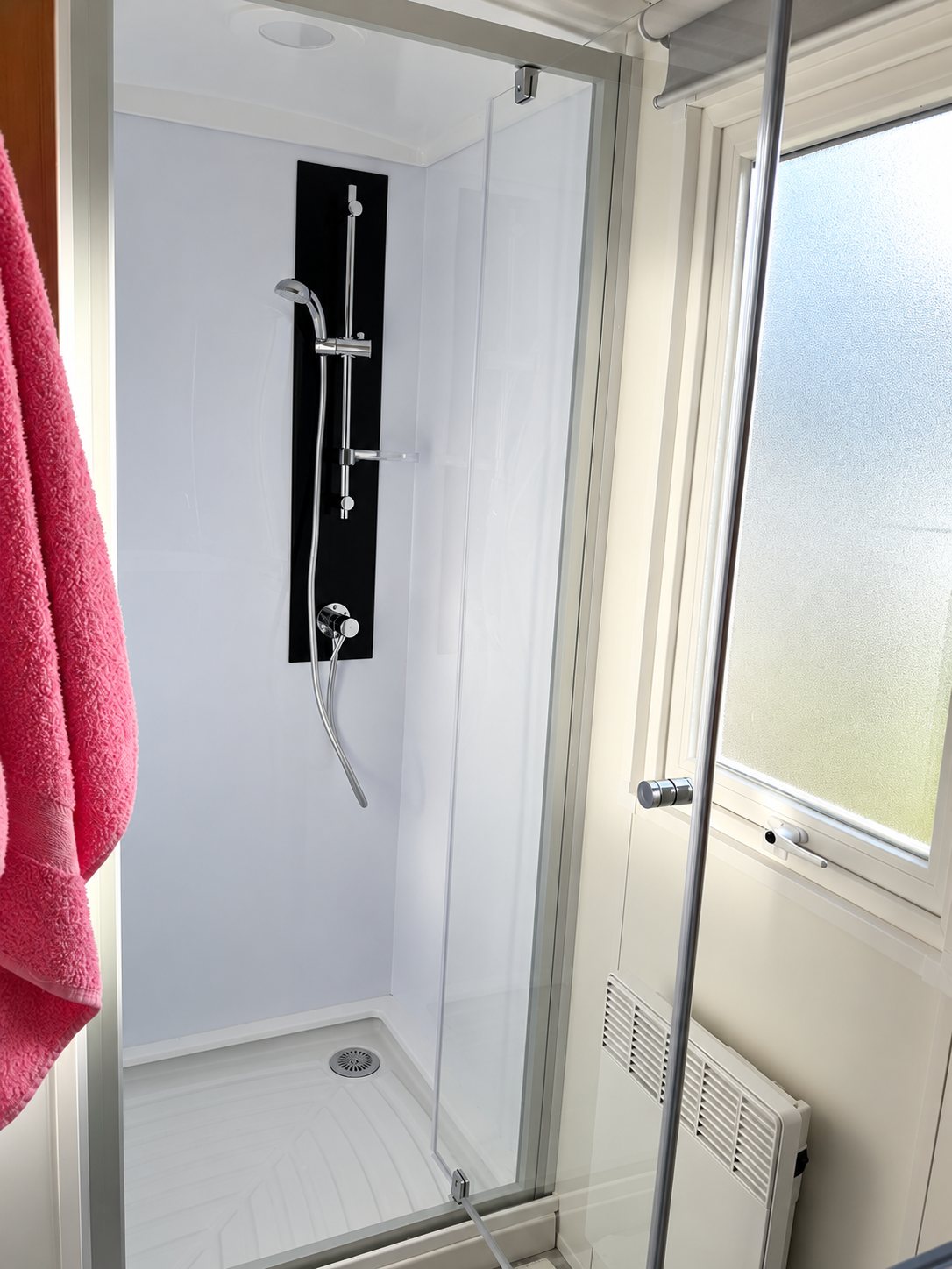 Cabine de douche à porte vitrée dans une salle d’eau compacte.