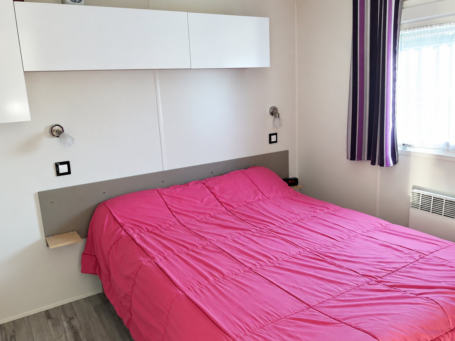Chambre avec lit double, couette rose et rangements.