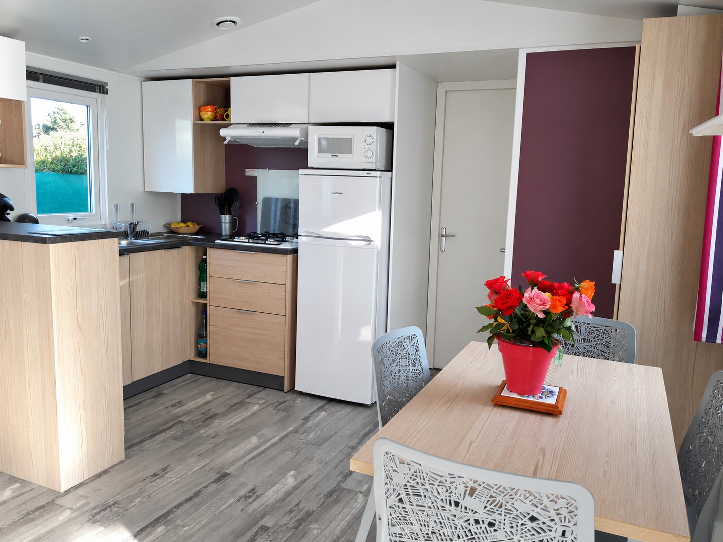 Cuisine et coin repas d’un mobil-home, avec un bouquet de roses sur la table.