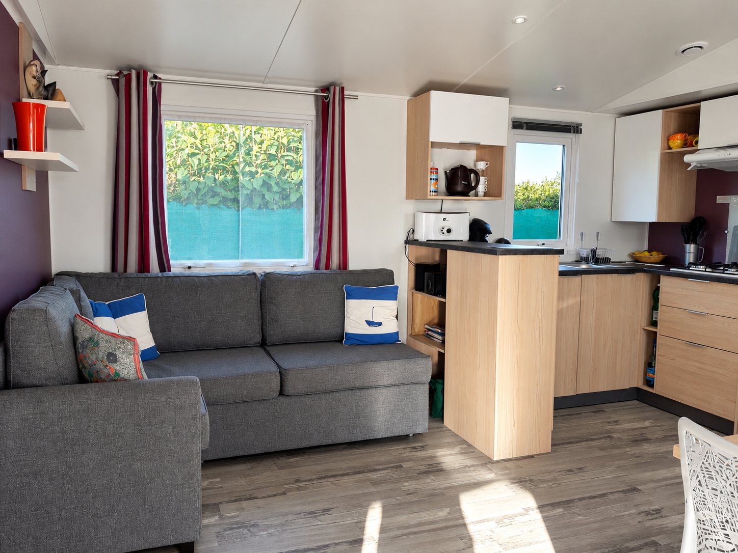 Salon avec canapé gris et cuisine ouverte dans un mobil-home.