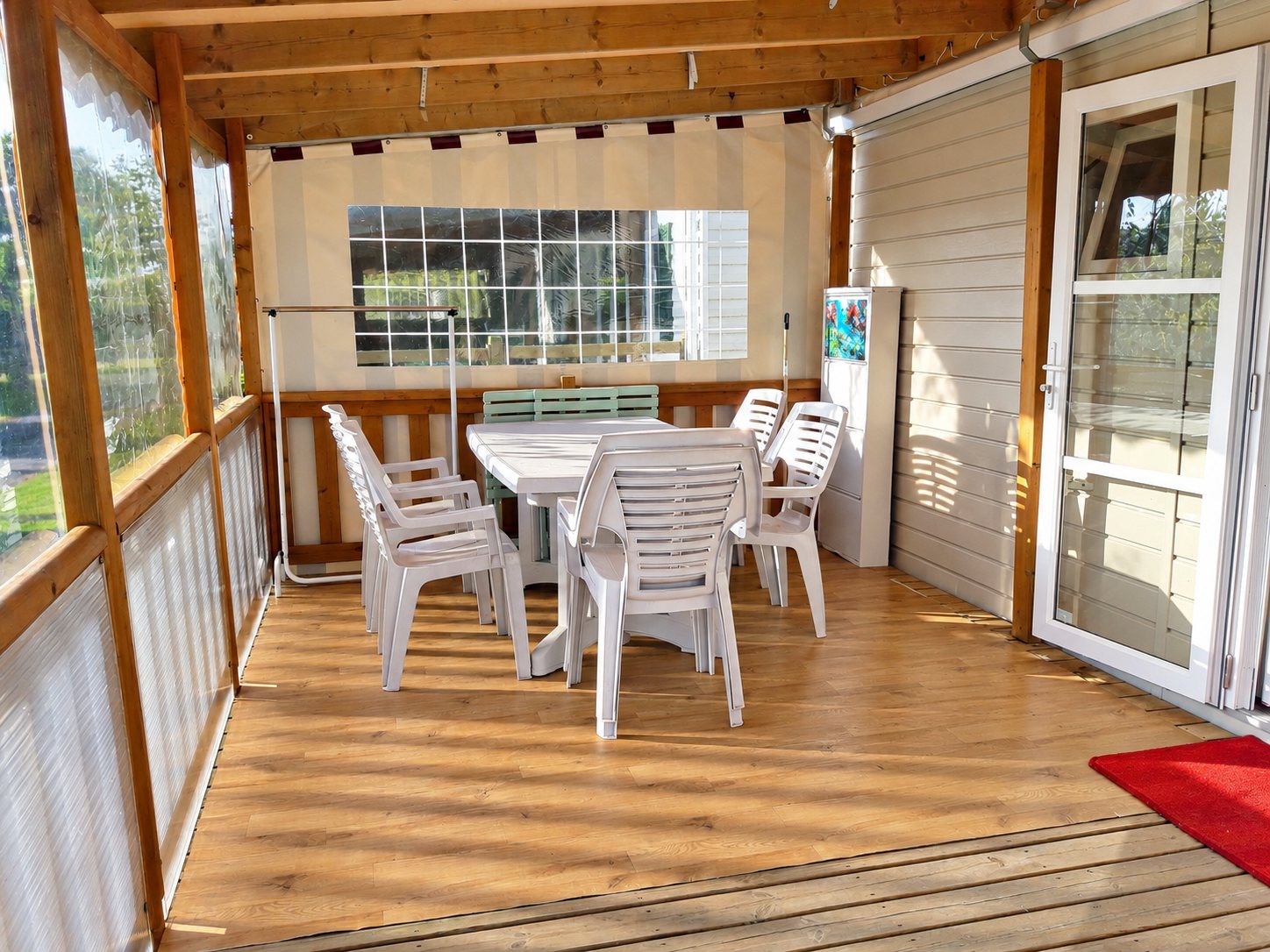 Terrasse couverte d’un mobil-home avec une table et des chaises blanches.